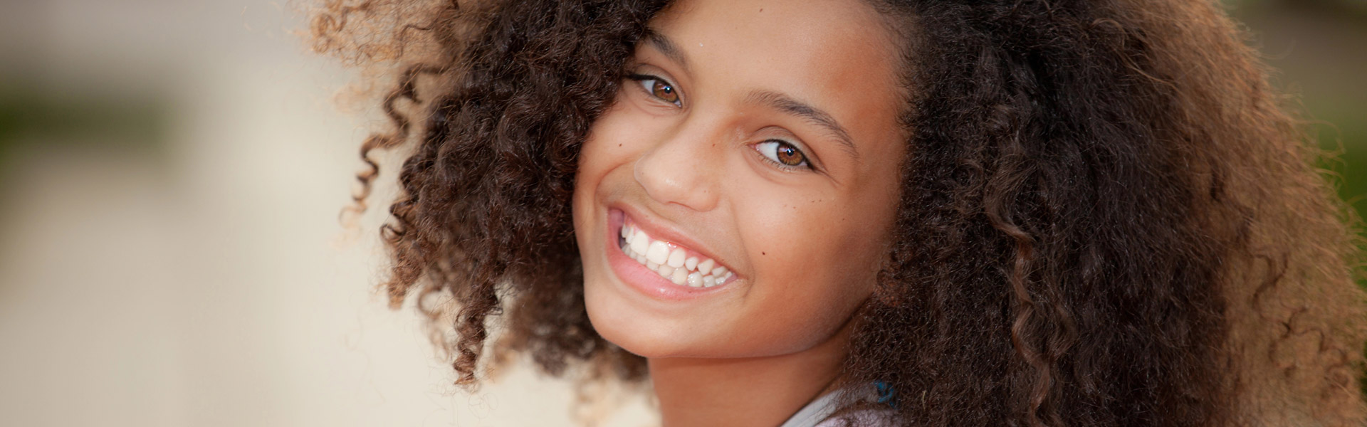 Young girl with curly hair smiling, reflecting healthy childhood dental habits